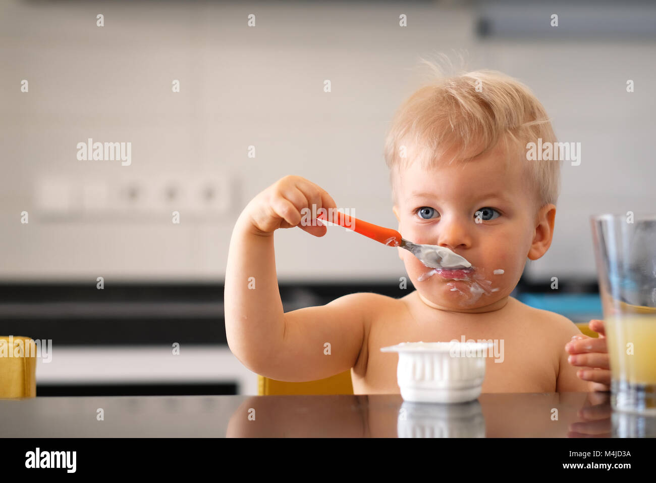 Adorable one year old baby boy eating yoghurt with spoon Stock Photo