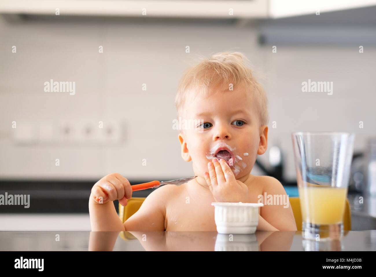 Adorable one year old baby boy eating yoghurt with spoon Stock Photo