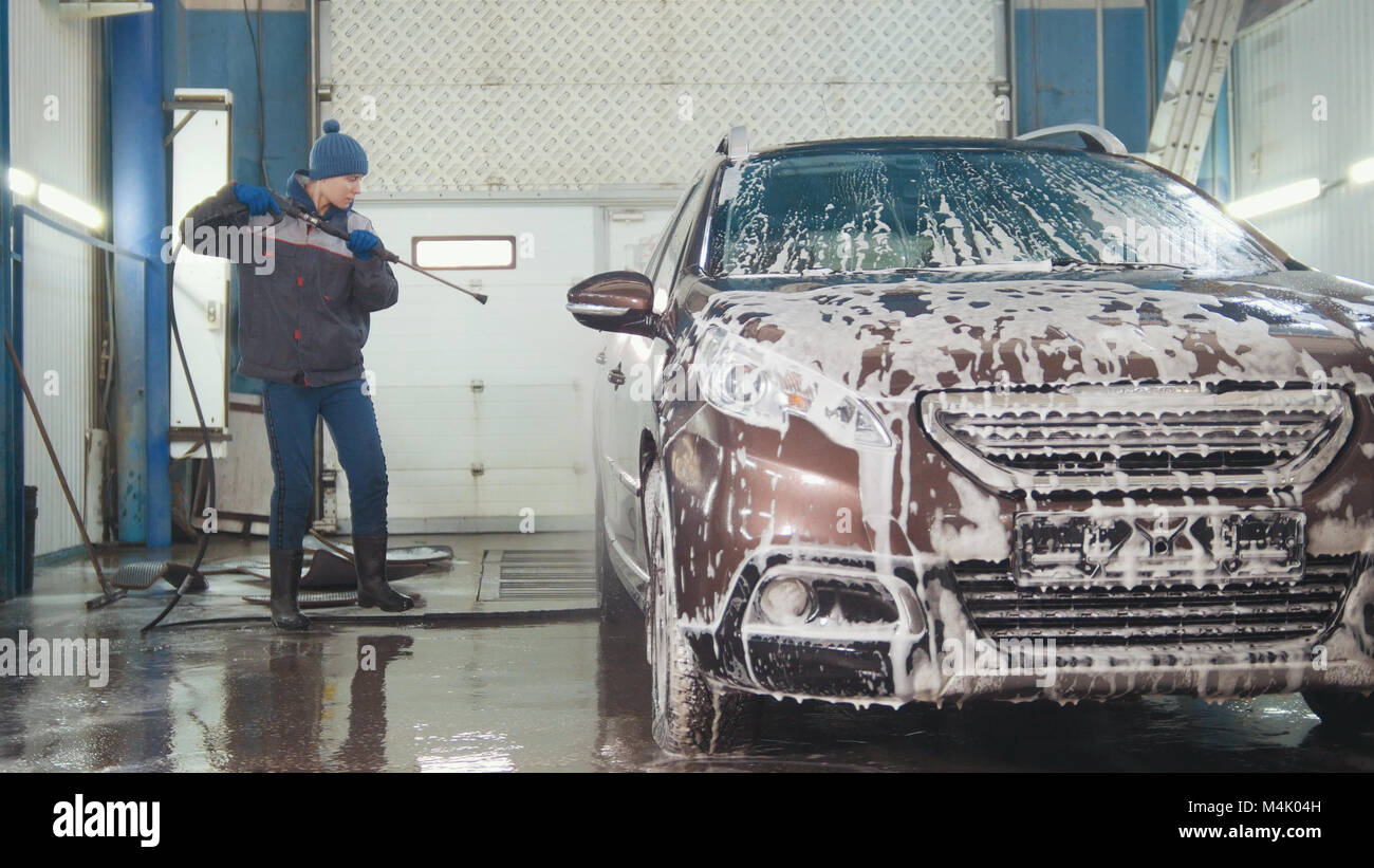 Worker in auto service is washing a car in the suds by water hoses