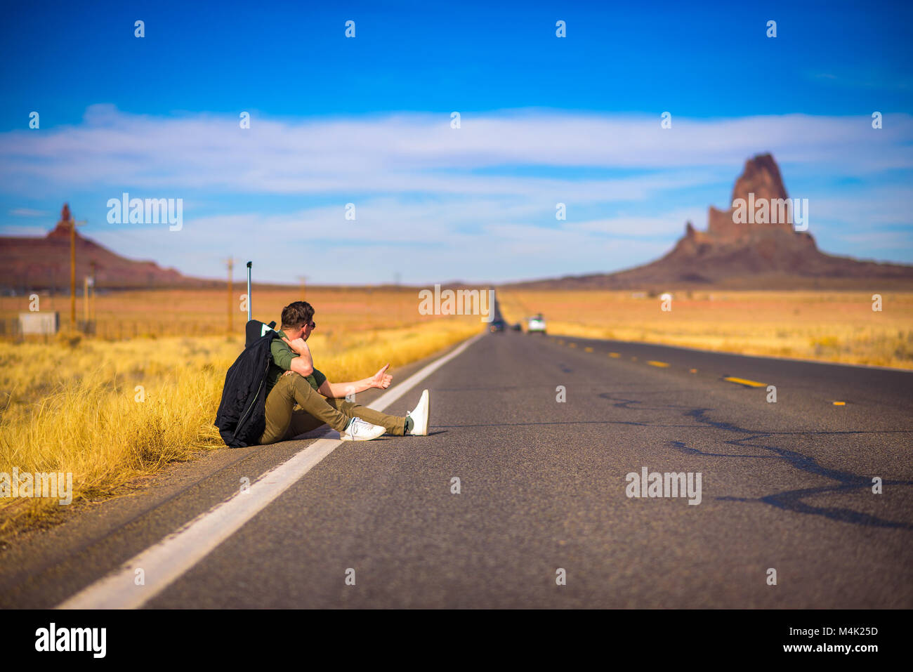 Tired hitch-hiker with suitcase sitting on a road Stock Photo