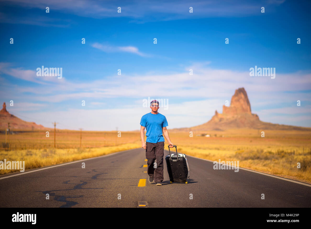 Young traveler with a suitcase walking on a road in Arizona Stock Photo
