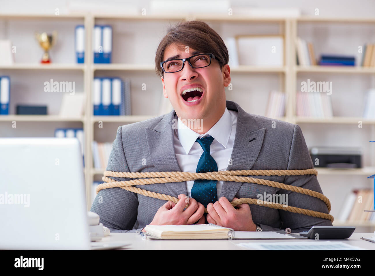 Businessman tied up with rope in office Stock Photo Alamy