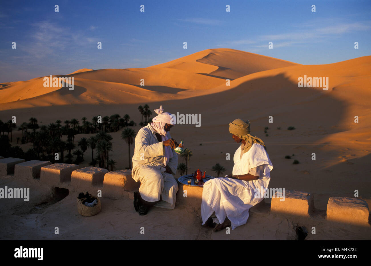 Algeria. Taghit or Tarit. Western Sand Sea. Grand Erg Occidental. Sahara desert. Sand dunes. Sand sea. Oasis. Men having tea, palm trees. Stock Photo