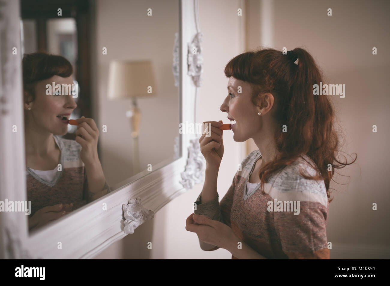 Woman applying lipstick in front of mirror Stock Photo