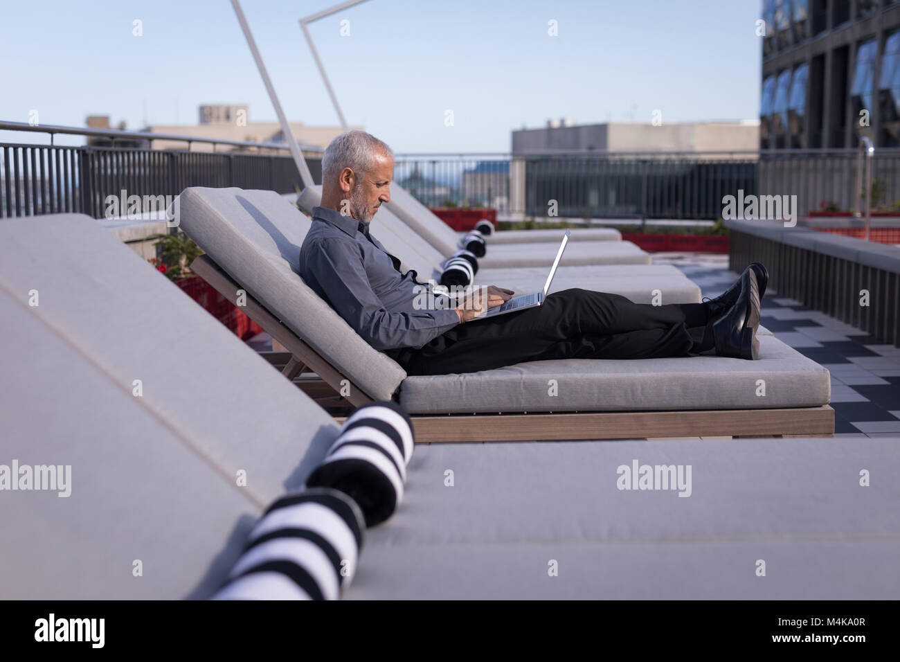 Businessman using a laptop while resting on a sun lounger Stock Photo