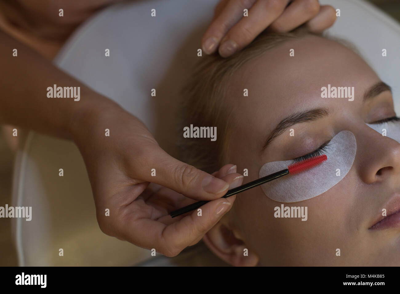 Beautician giving eyelash extension treatment to female customer Stock Photo