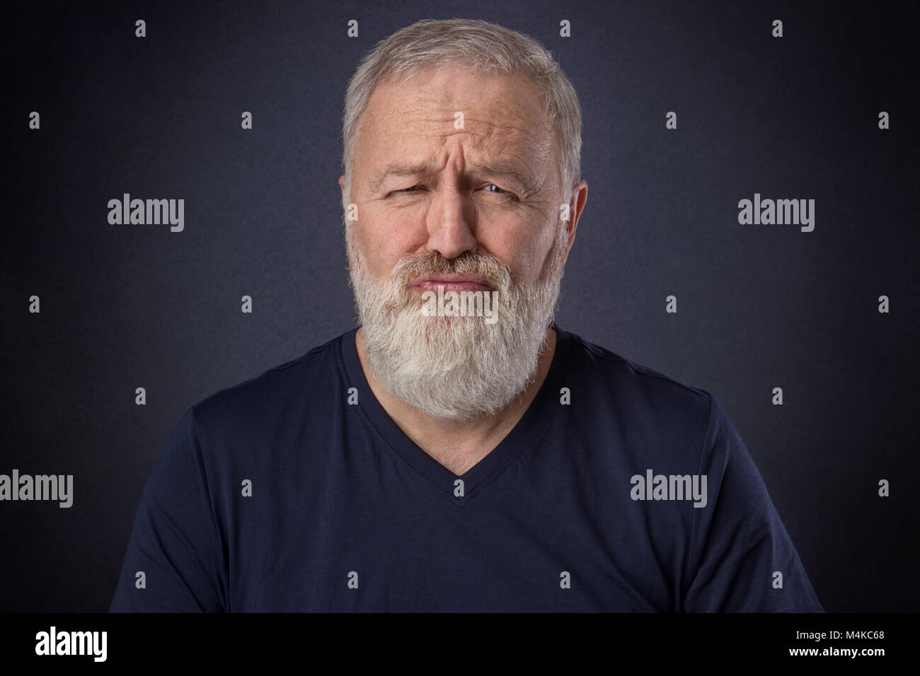 A 60 year old man with gray beard posing spoiled grimace in the studio Stock Photo