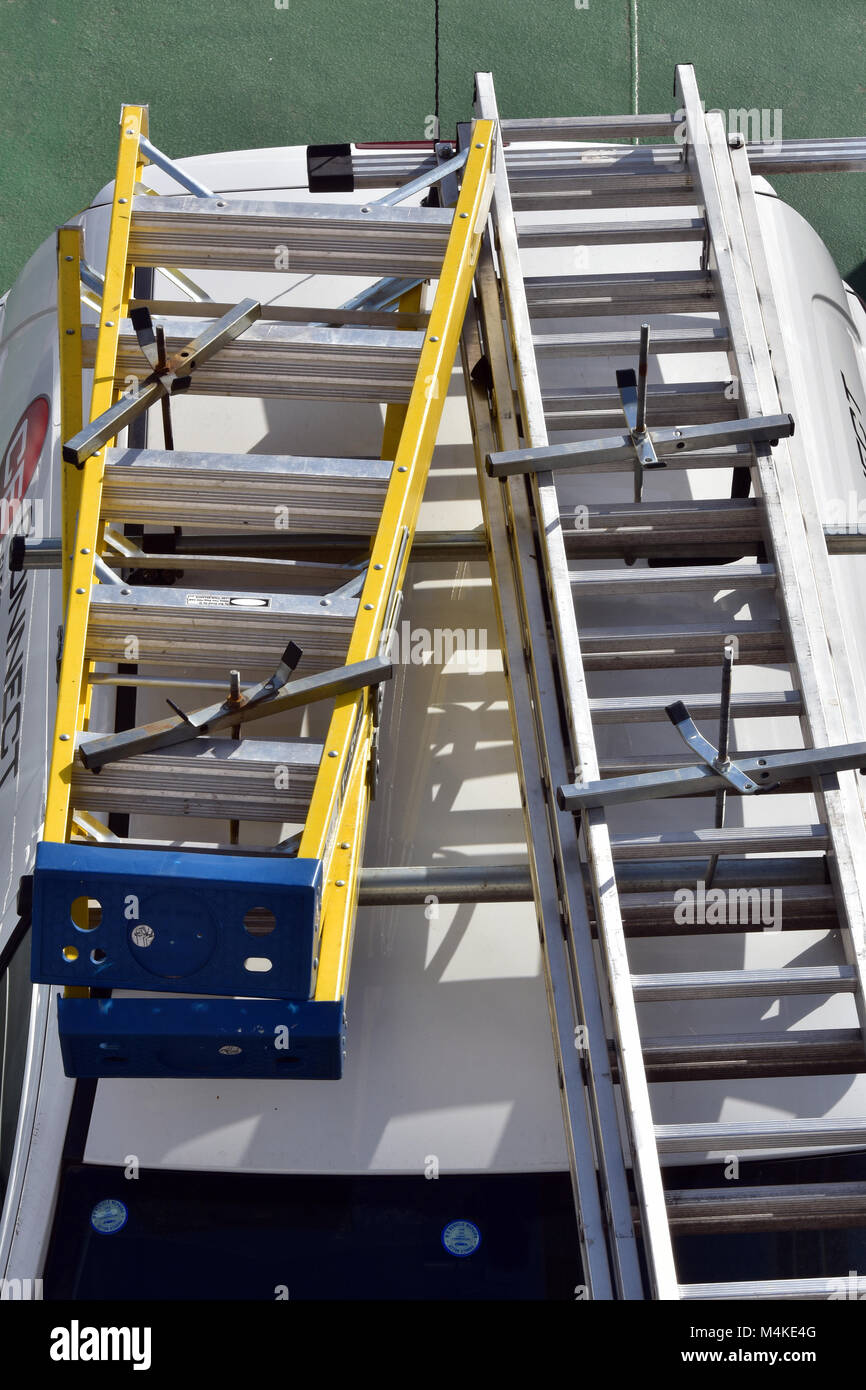 Ladders stored or secured to the roof of a tradesmans van or vehicle to keep from falling from the roof. Security of equipment on a vanstepladders. Stock Photo