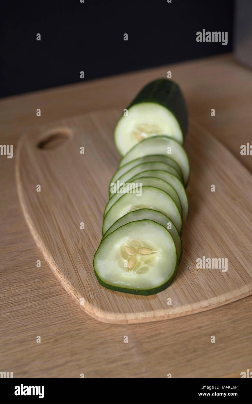 Cut-up Cucumber on a Light Wood Surface Near a Dark Wall Stock Photo