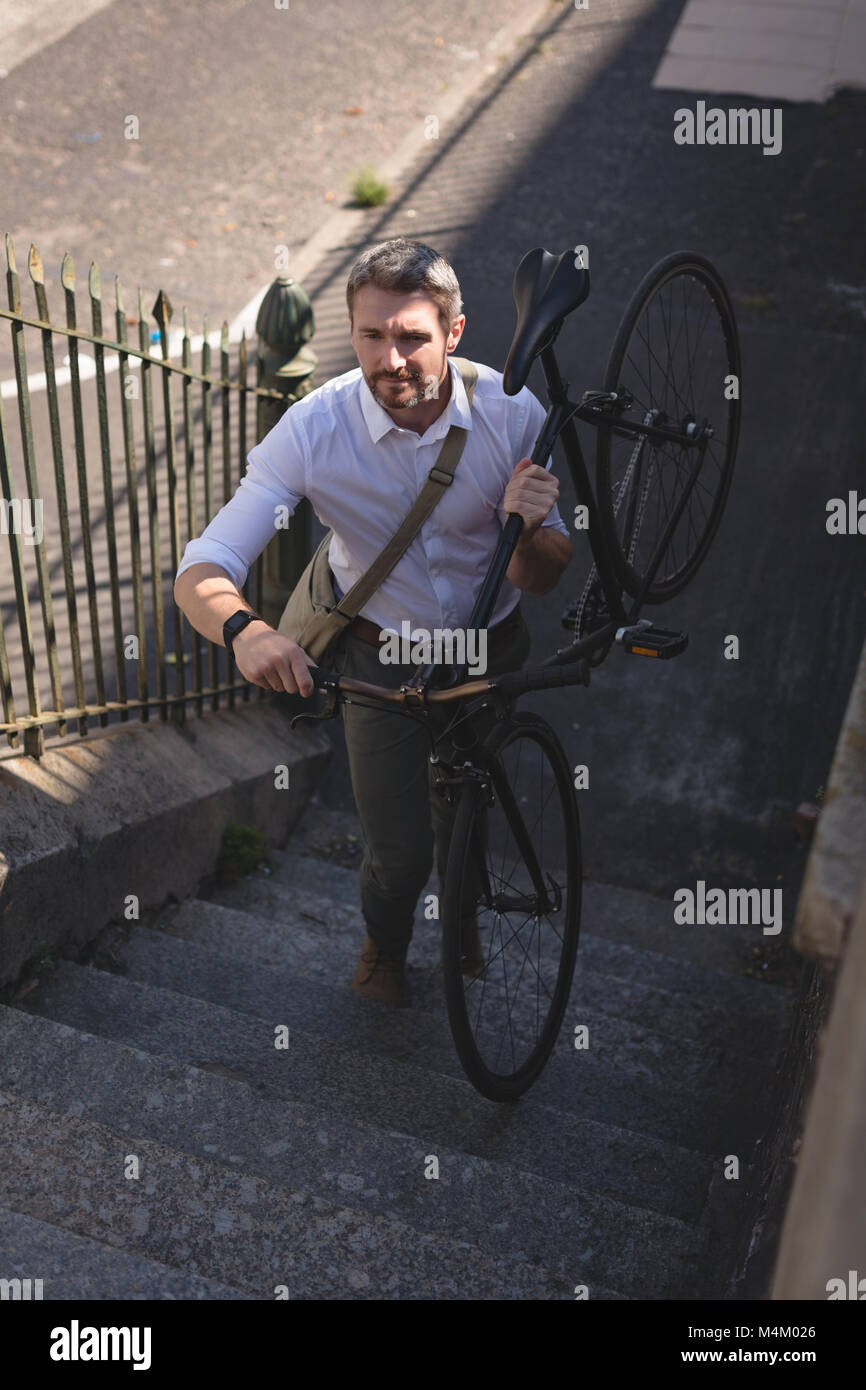 Man carrying bicycle and walking upstairs Stock Photo