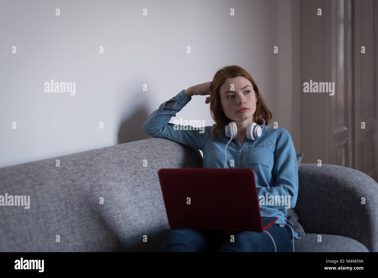 Thoughtful woman with laptop sitting on sofa in living room Stock Photo ...