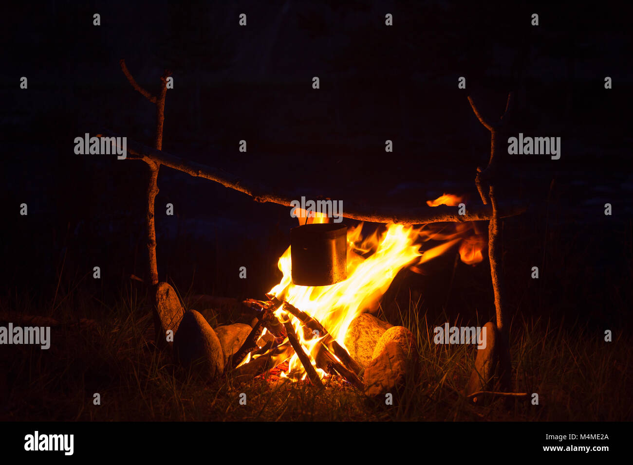 Cooking meal in a kettle on burning campfire in wild camping at night ...