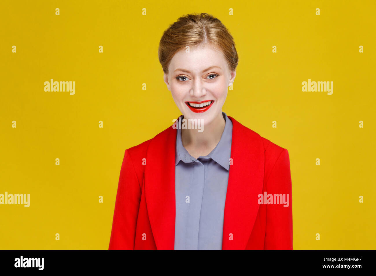 Ginger red head model in red suit toothy smile. Studio shot, isolated on yellow background Stock Photo