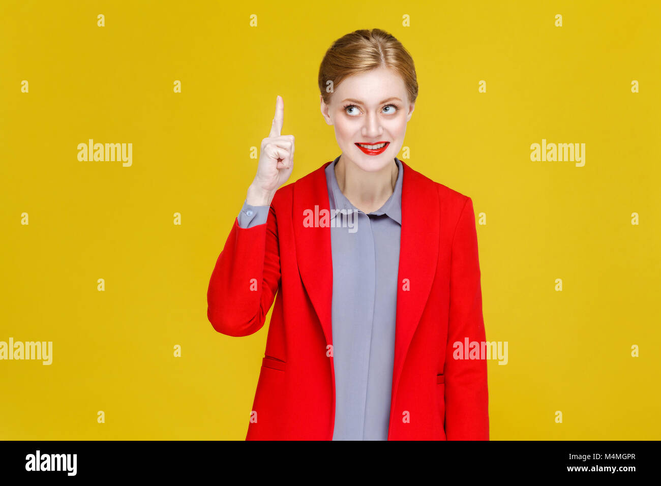 Ginger red head business woman in red suit have good plan, idea. Studio shot, isolated on yellow background Stock Photo