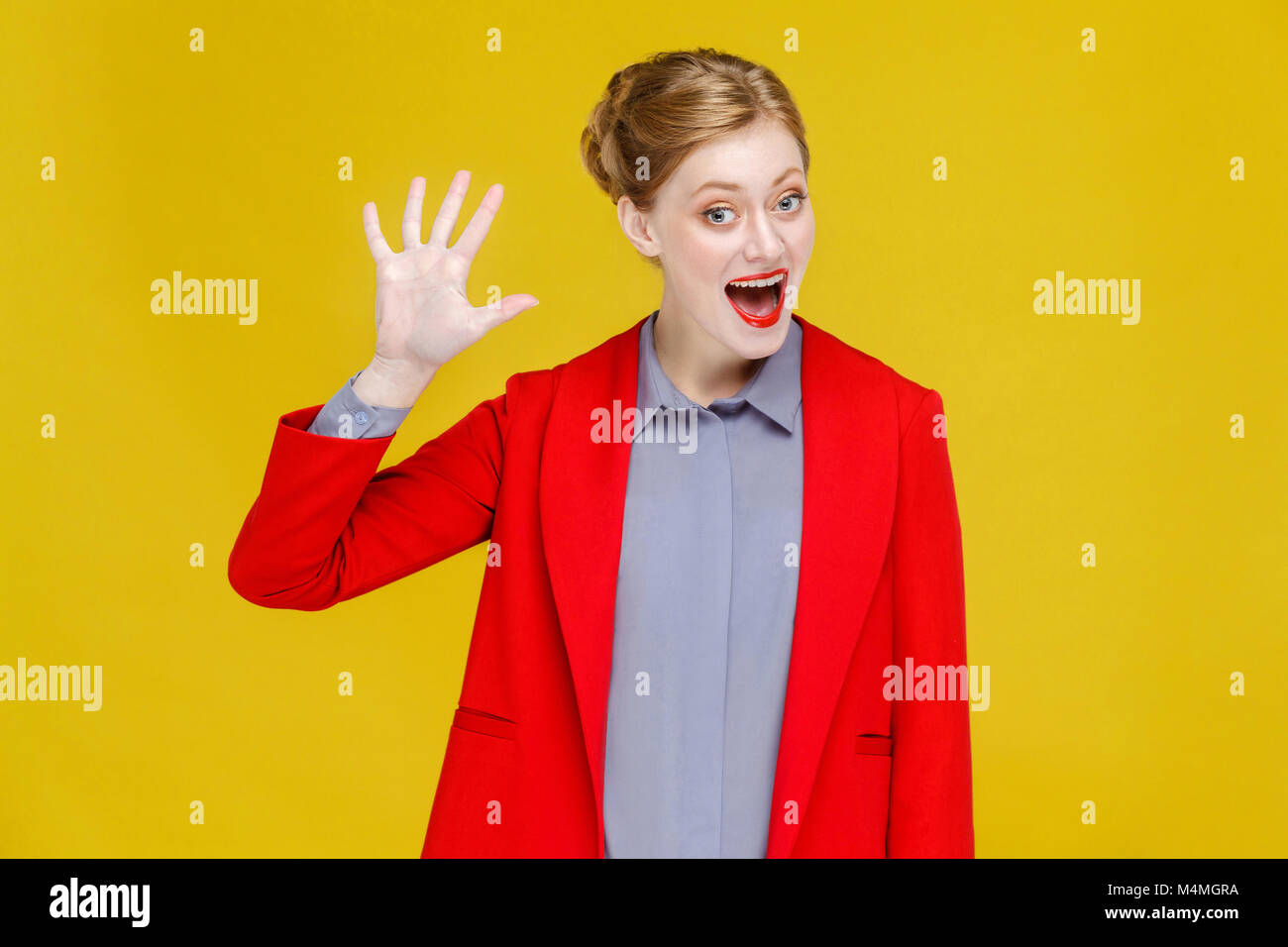 Hello! Ginger red head business woman in red suit showing hi sign. Studio shot, isolated on yellow background Stock Photo