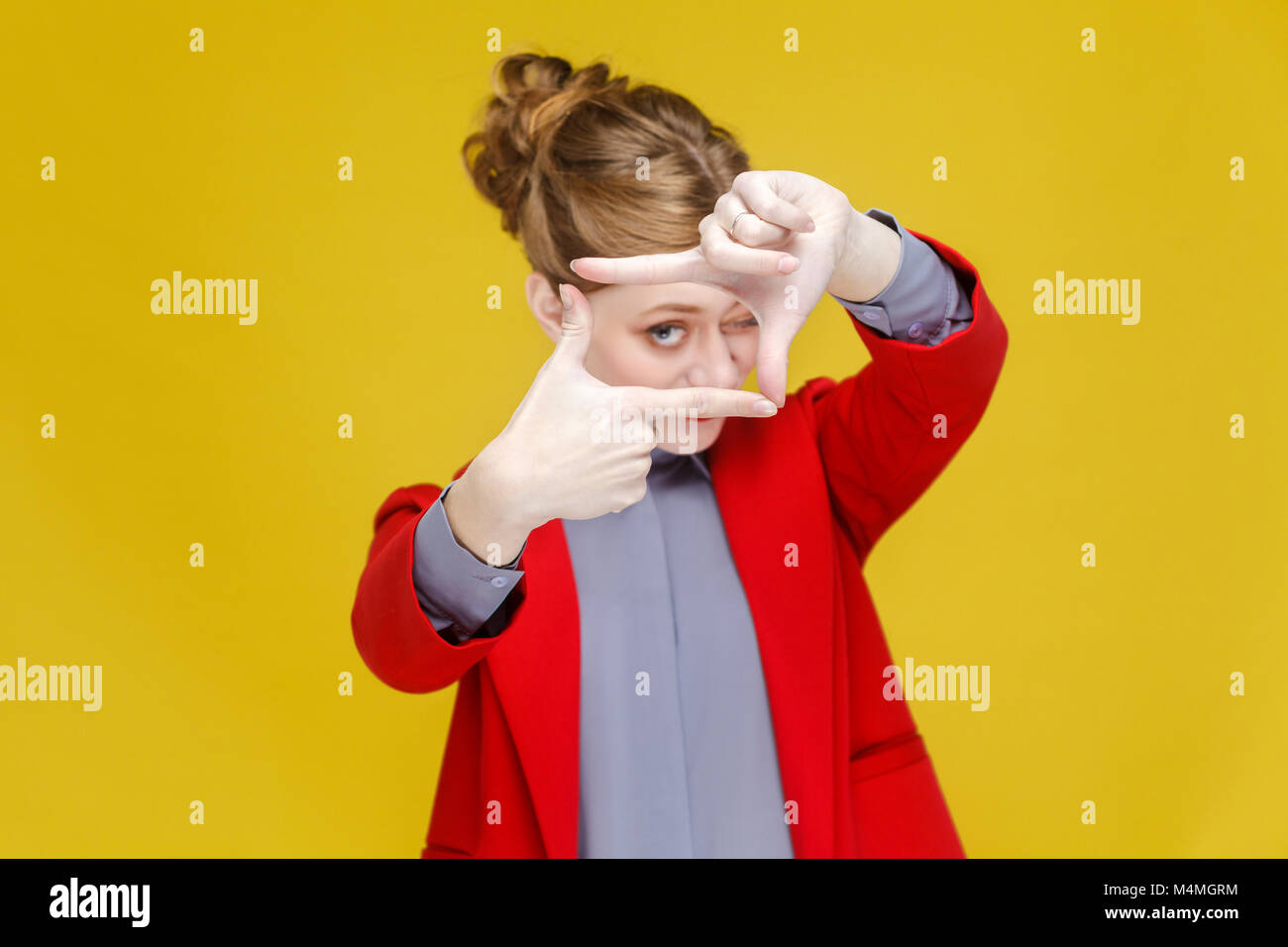Red head business woman in red suit showing frame,crop sign. Studio shot, isolated on yellow background Stock Photo