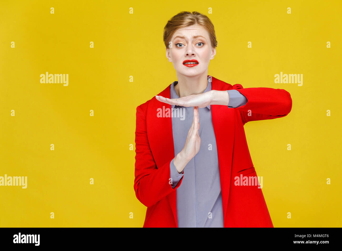 Time out! Unhappy business woman in red suit showing pause sign. Studio shot, isolated on yellow background Stock Photo