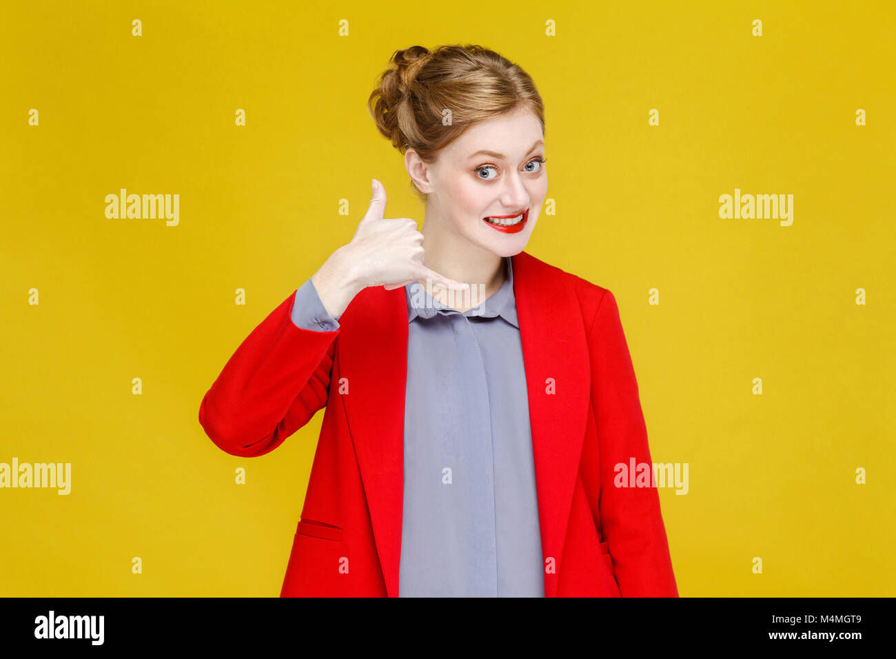 Ginger red head woman in red suit showing phone sign. Studio shot, isolated on yellow background Stock Photo