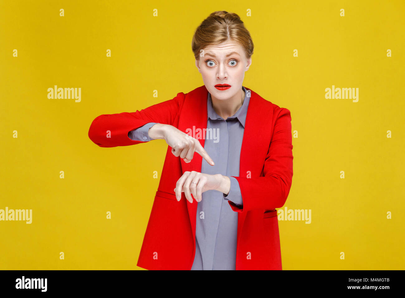 No time! Ginger red head woman in red suit showing at watch. Studio shot, isolated on yellow background Stock Photo