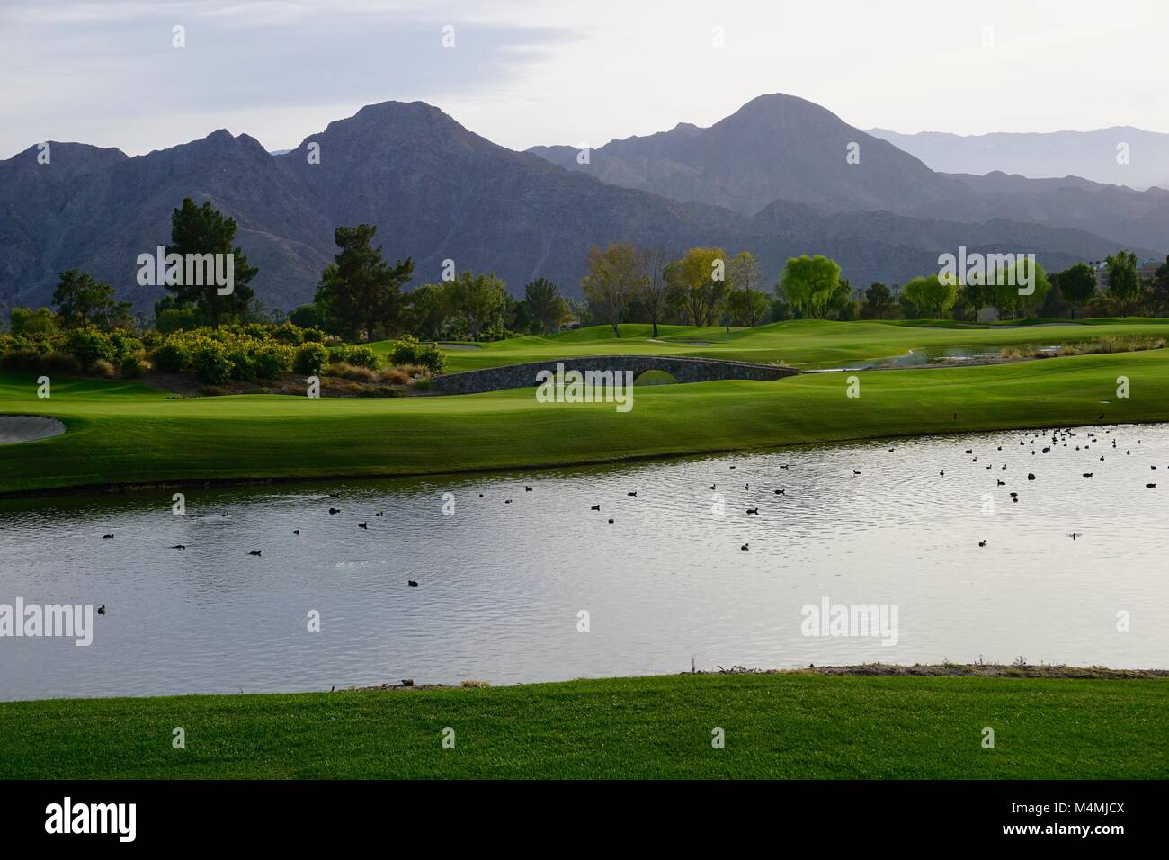 Golf course landscape including bridge and water in front of mountain background Stock Photo