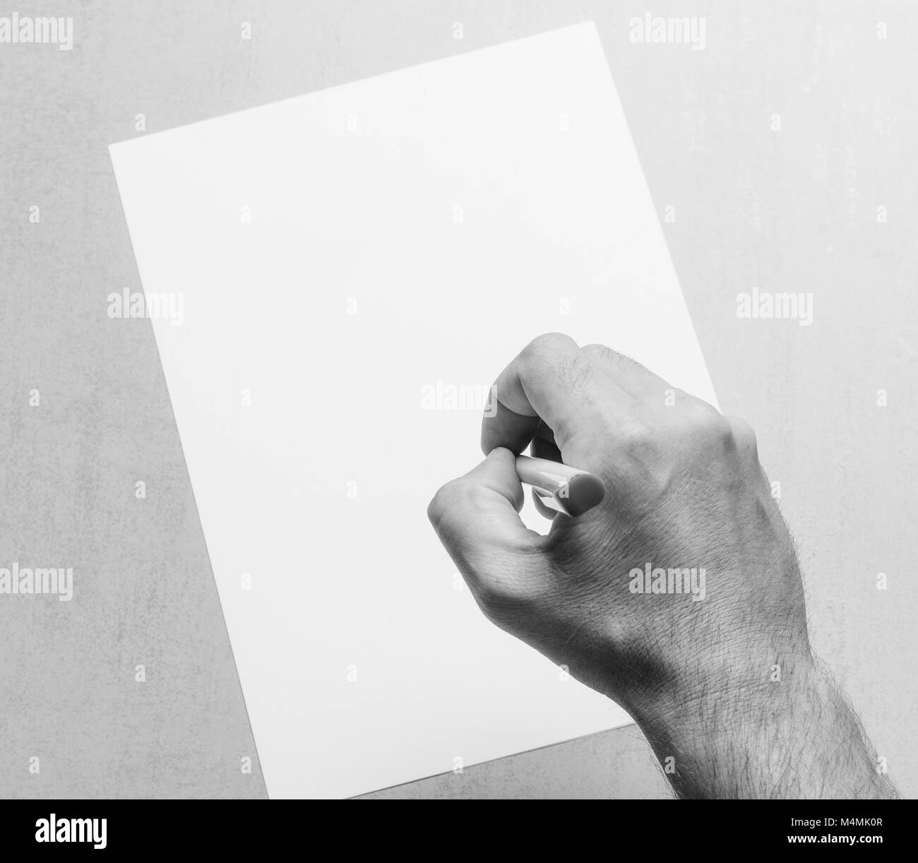 Mans hand with a ballpoint pen and blank white sheet of paper on a gray ...