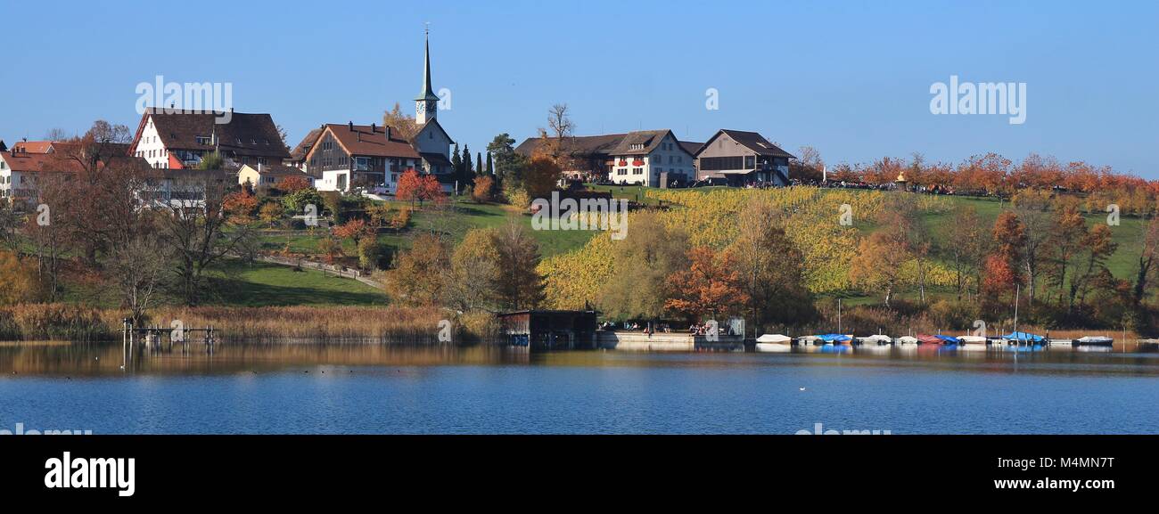 Idyllic village Seegraben in autumn. Fishing boats on lake Pfaffikersee. Colorful trees and fields. Stock Photo