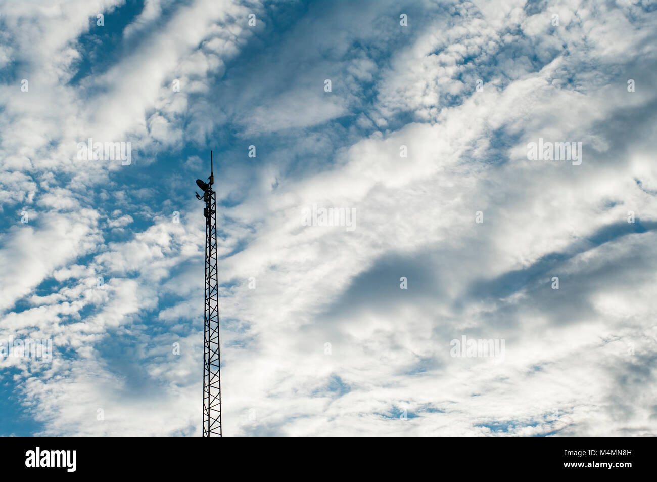 Silhouette of upper part of radio tower against a backdrop of cirrus clouds in blue sky Stock Photo