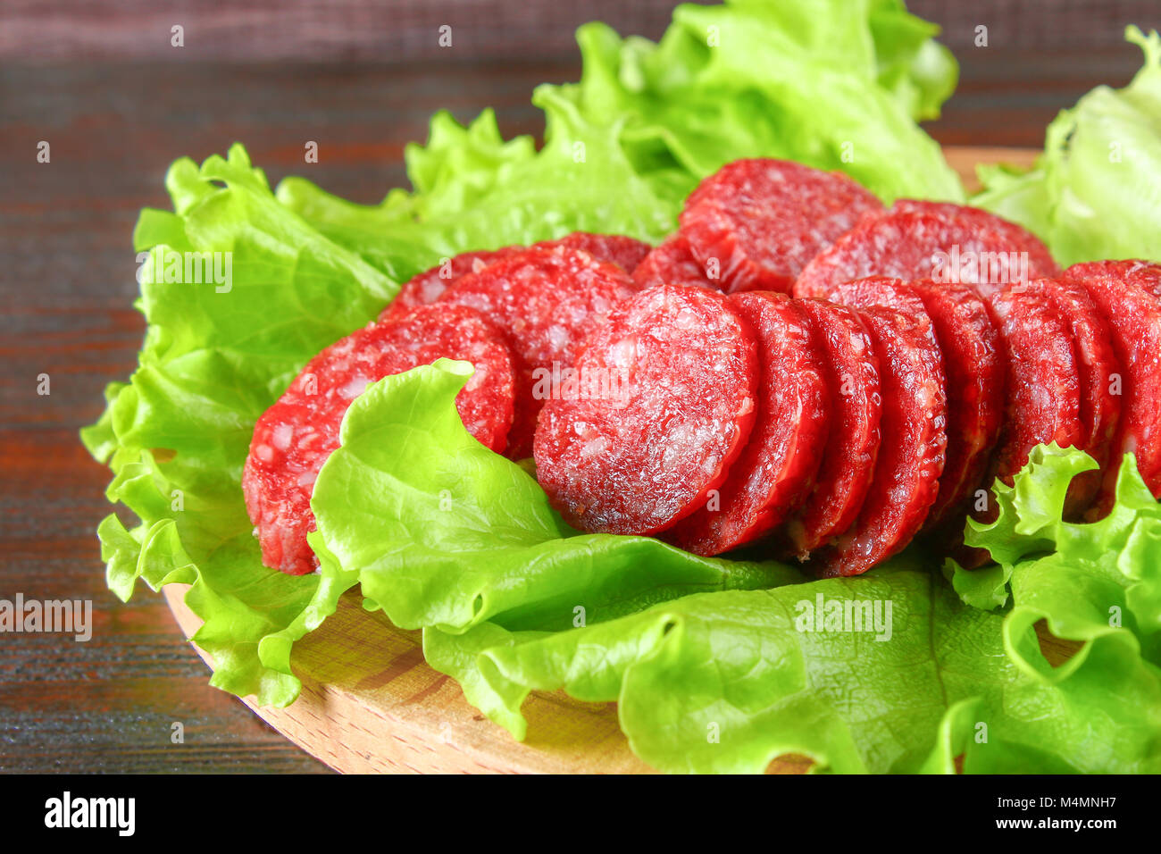 Smoked sausage, salami chopped in slices on a salad on a wooden circular cutting board on a brown table Stock Photo