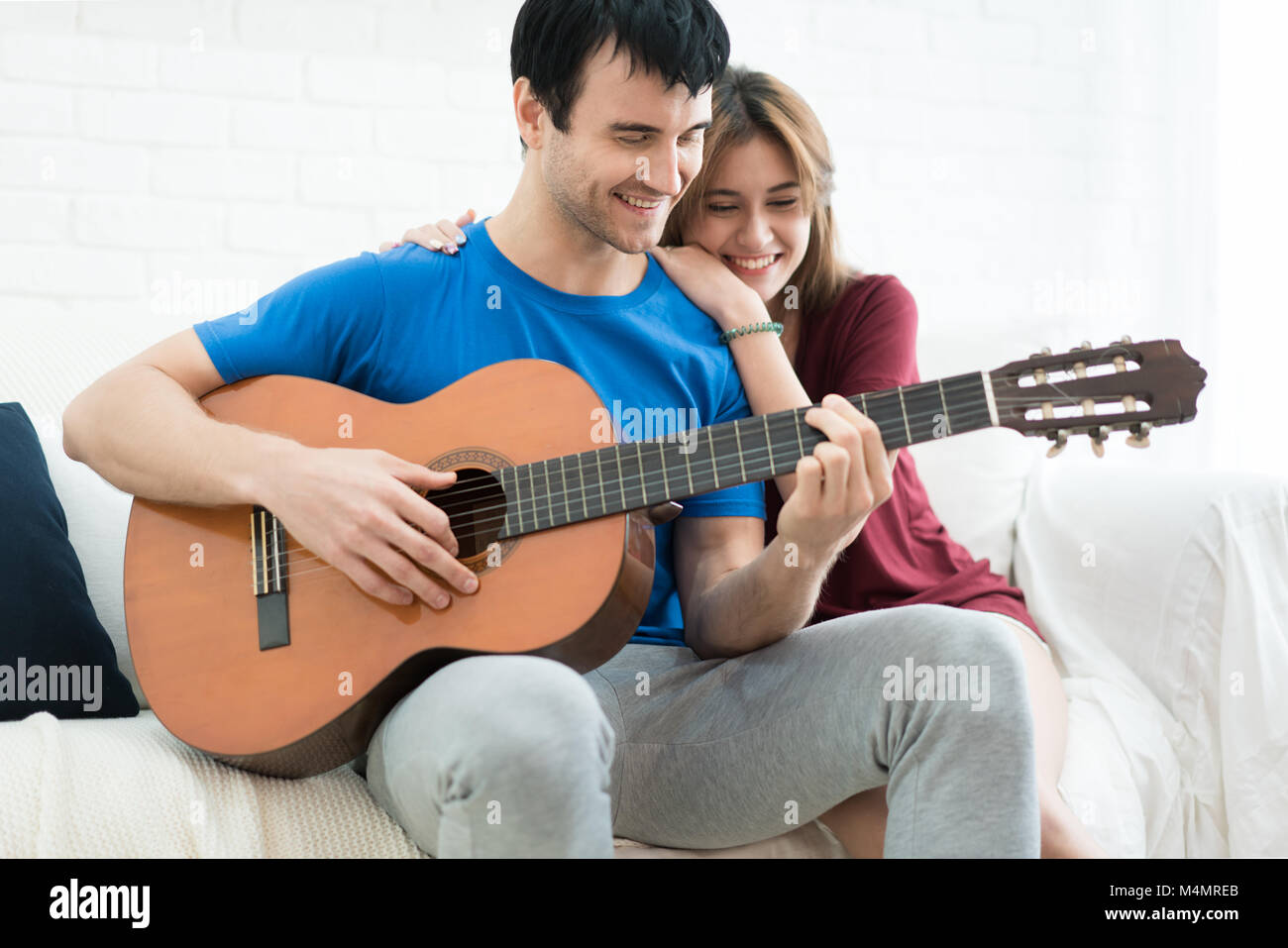 Lover couple young man resting at home and playing guitar for his girlfriend in bed. Happy couple in home. Stock Photo