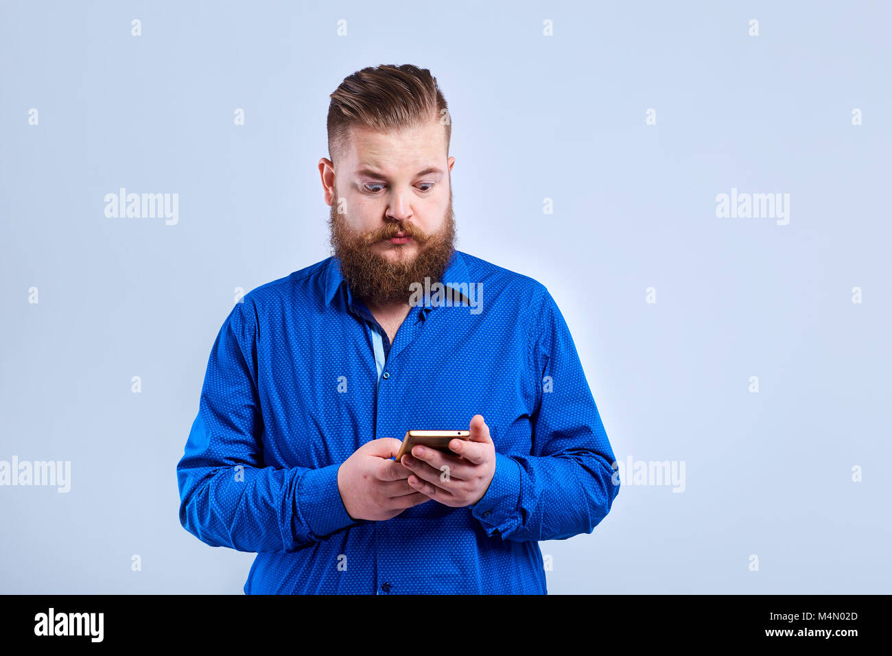 A fat, bearded man looks at the phone  with a surprised expressi Stock Photo