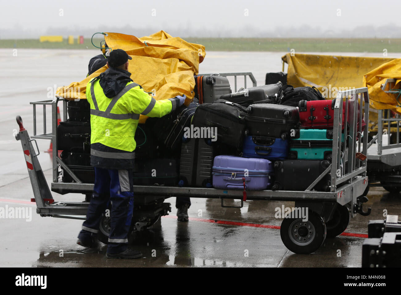 Airport workers cover passengers' luggage from the rain on a cart near the airplane. Stock Photo