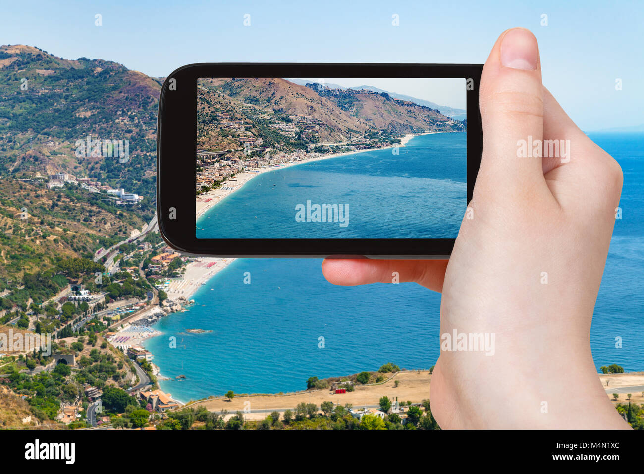 travel concept - tourist photographs Letojanni resort town of coast of Ionian Sea from Taormina city in Sicily Italy in summer on smartphone Stock Photo
