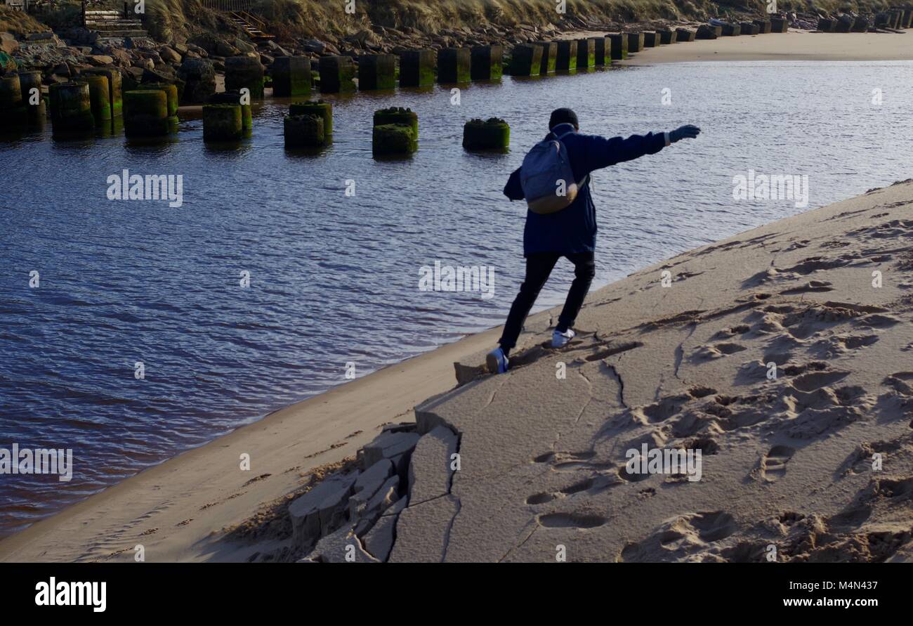 Young Man Collapsing the Sandy Bank of the Coastal River at Cruden Bay. Aberdeenshire, Scotland, UK. Stock Photo