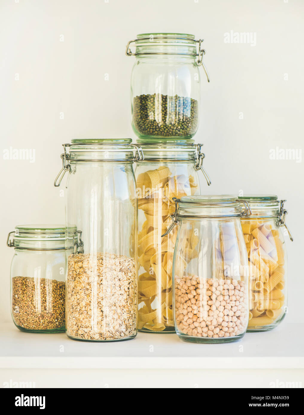 Various raw cereals, grains, beans and pasta for healthy cooking in glass jars on kitchen shelf