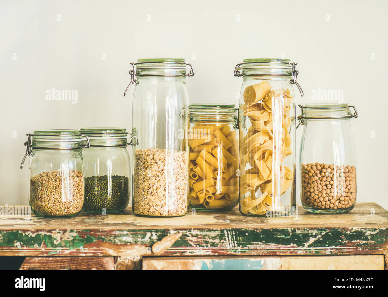 Various uncooked cereals, grains, beans and pasta for healthy cooking in glass jars on rustic