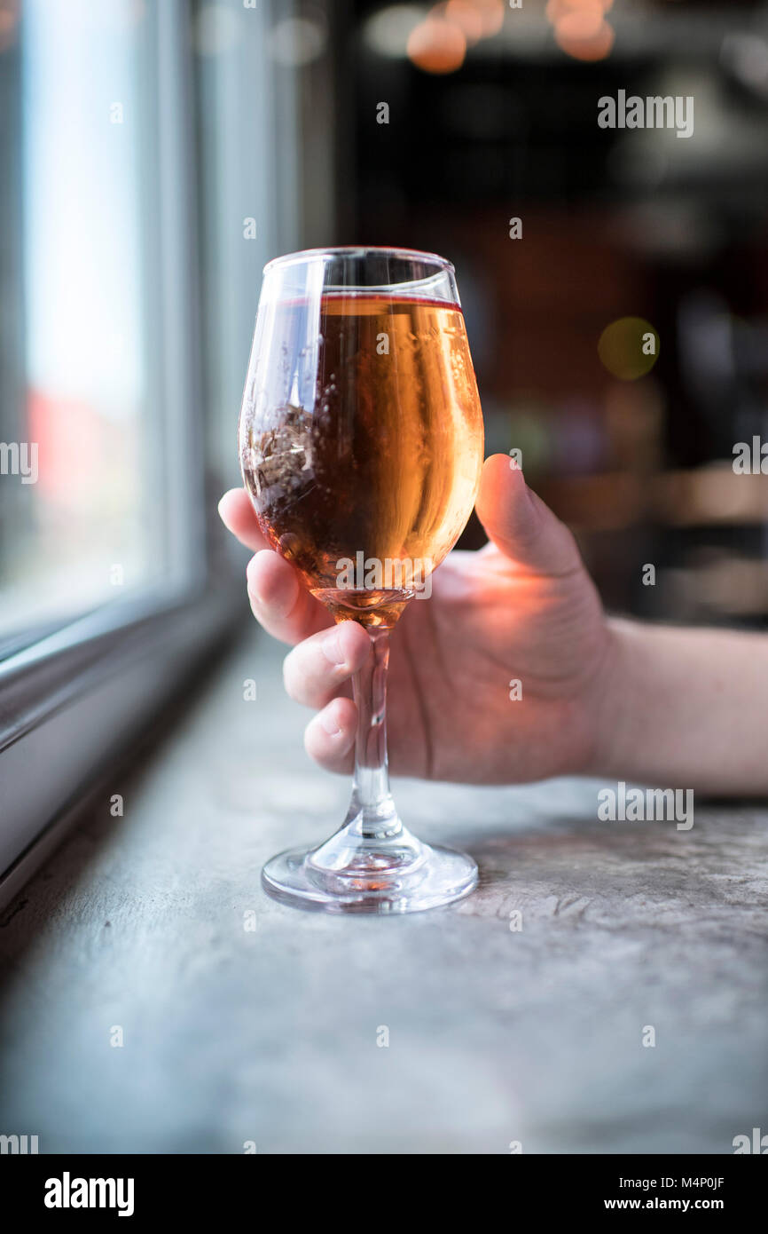 Glass of cider beer being held by a man at a modern, beautiful, natural light bar. Stock Photo