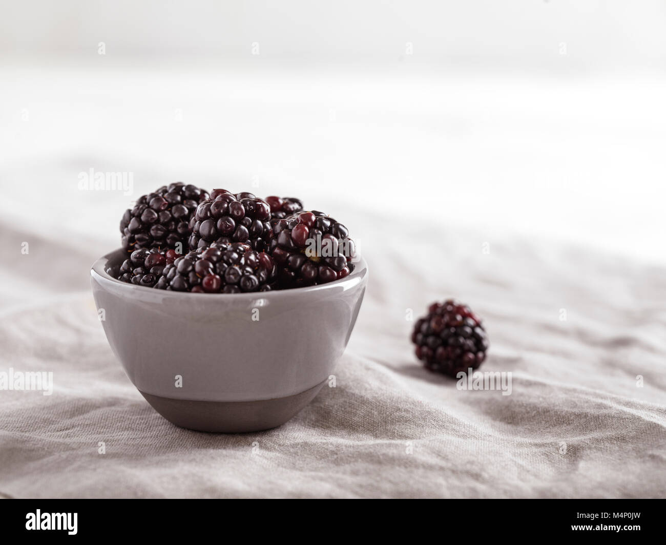 Small, gray bowl filled with fresh blackberries on a gray linen with a bright, airy background. Stock Photo