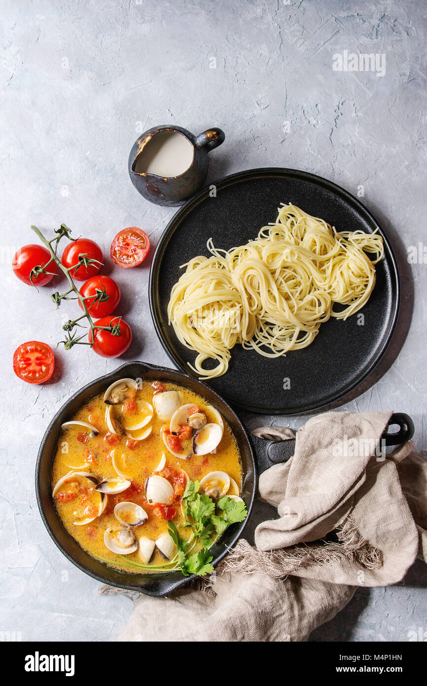 Vongole in tomato cream sauce for pasta in cast-iron pan with textile and black plate with cooked spaghetti over gray texture background. Top view, sp Stock Photo