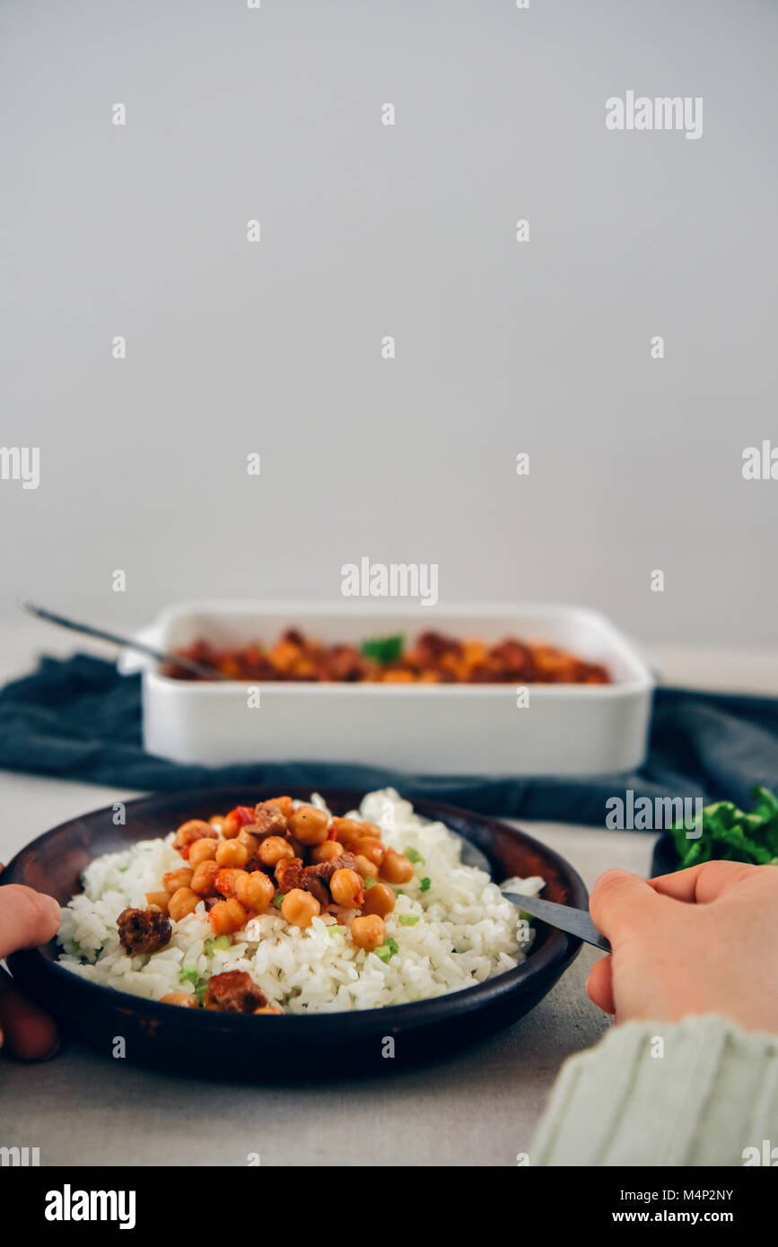 A woman eating fried rice topped with some garbanzo beans and beef stew