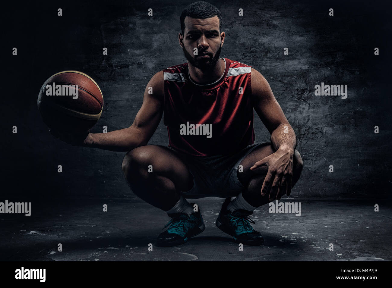 Full body portrait of a black basketball player sits on a floor and