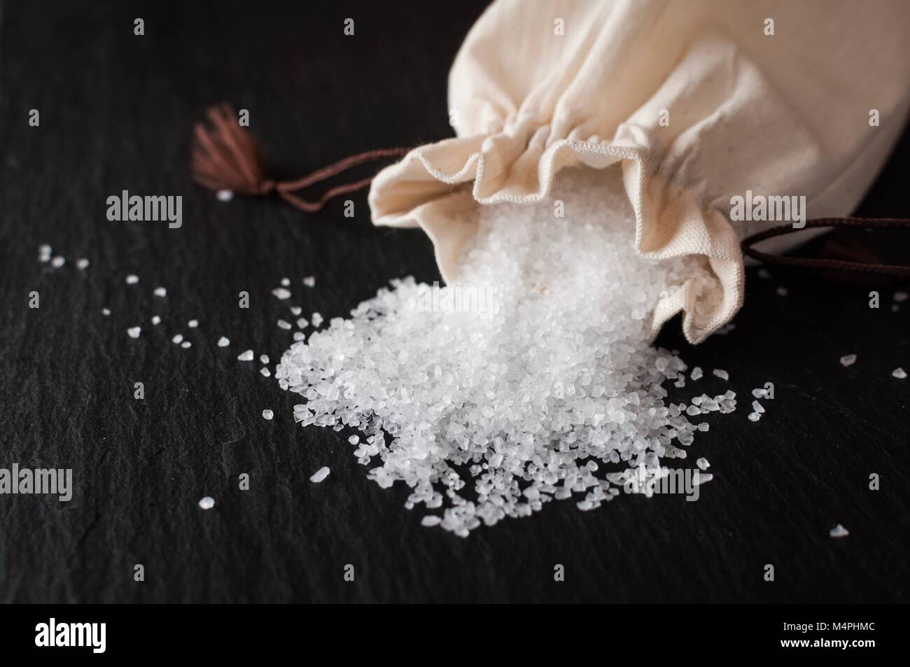 Rock salt spilling out of a small pouch onto a black slate Stock Photo