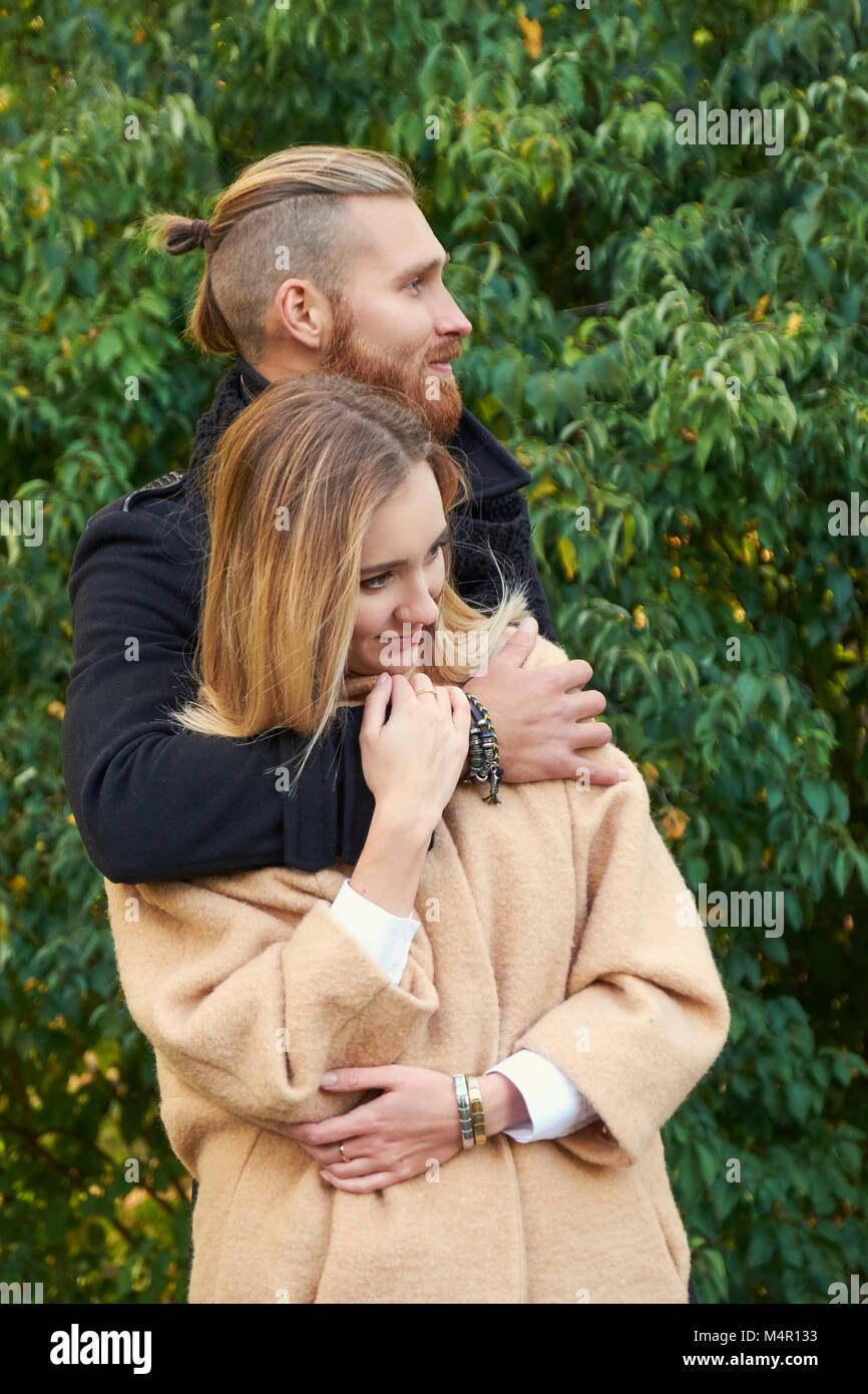 Portrait of couple on the date. Redhead bearded male hugging cute blonde female in an autumn park. Stock Photo