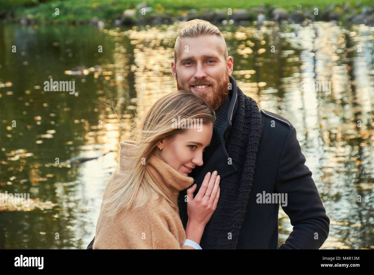 Portrait of couple on the date. Redhead bearded male hugging cute blonde female in an autumn park. Stock Photo