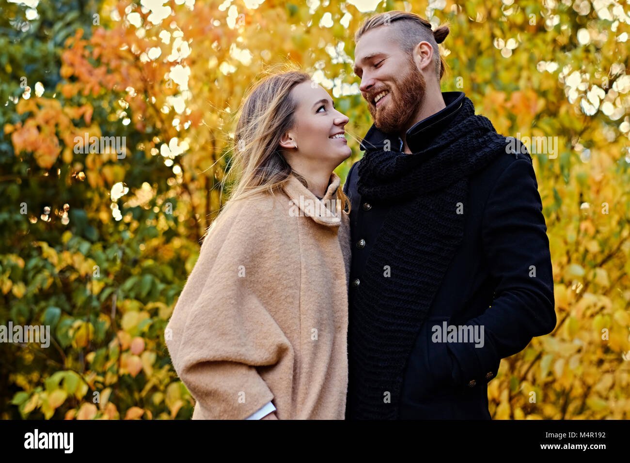 Autumn Love story. Redhead bearded male hugs the cute blonde female on the date in an autumn park. Stock Photo