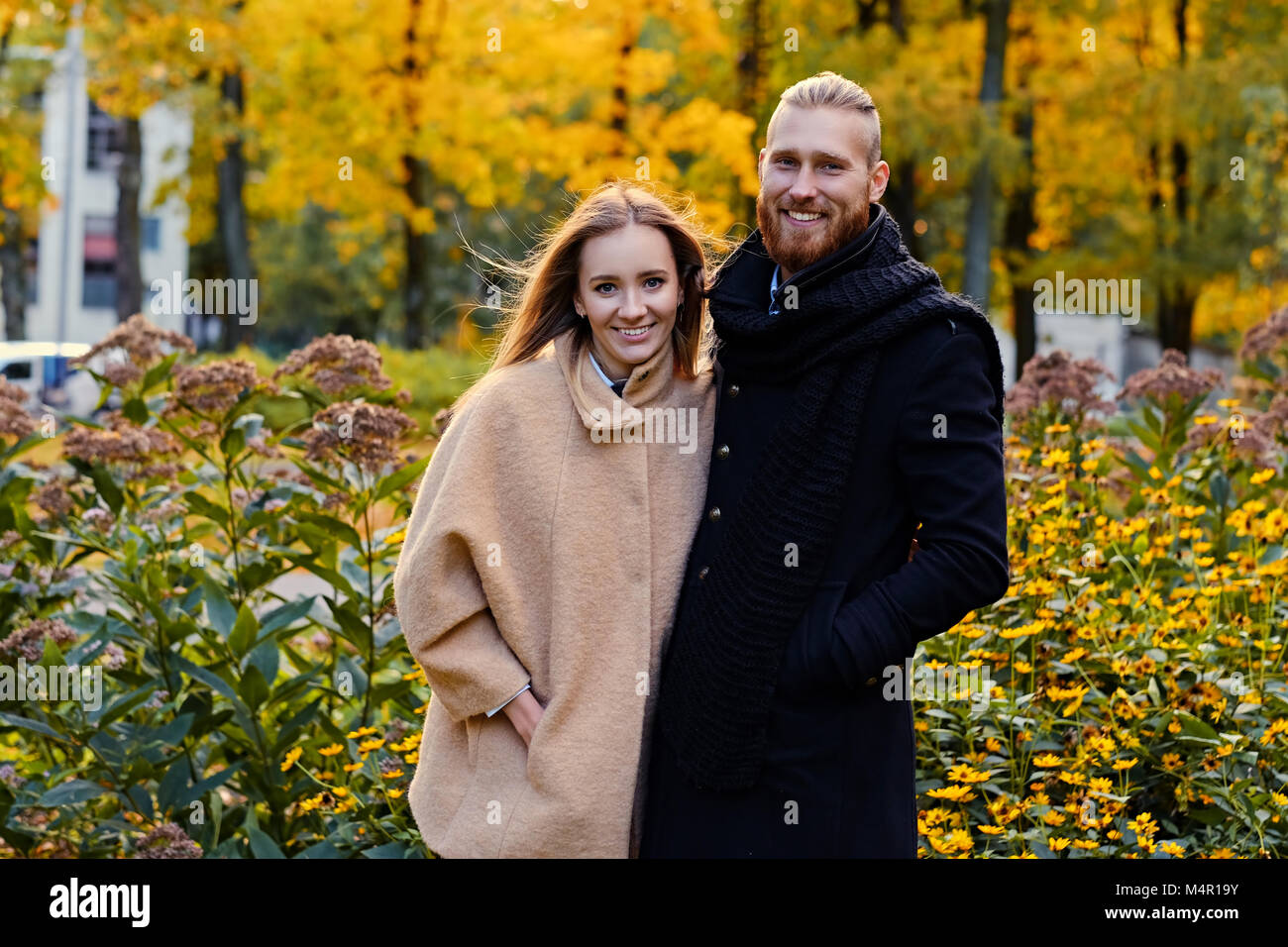 Autumn Love story. Redhead bearded male hugs the cute blonde female on the date in an autumn park. Stock Photo