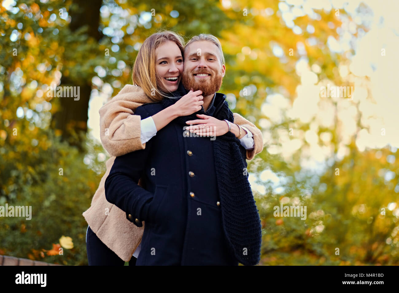 Autumn Love story. Redhead bearded male hugs the cute blonde female on the date in an autumn park. Stock Photo