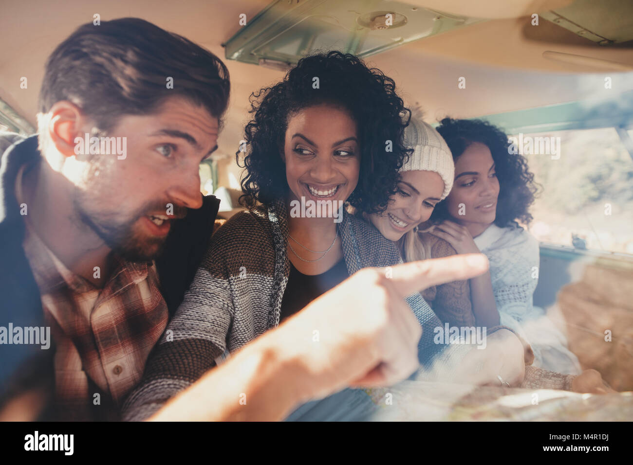 Friends on roadtrip sitting inside van and using map for directions. Group of man and women travelling together. Stock Photo