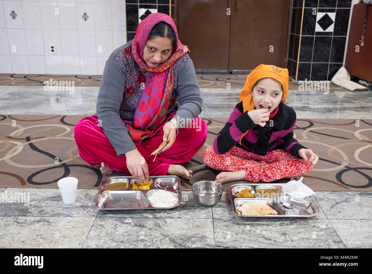 An Indian Sikh woman and her daughter eat together at the Baba Makhan Shah Lobana Sikh Center on 101 Avenue in Richmond Hill, Queens, New York City Stock Photo