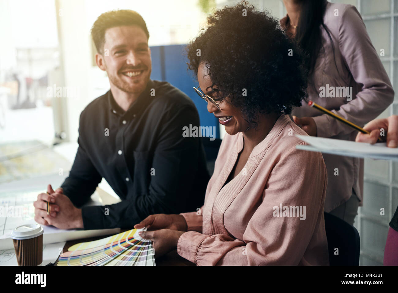 Smiling group of diverse designers sitting together at a desk in a ...