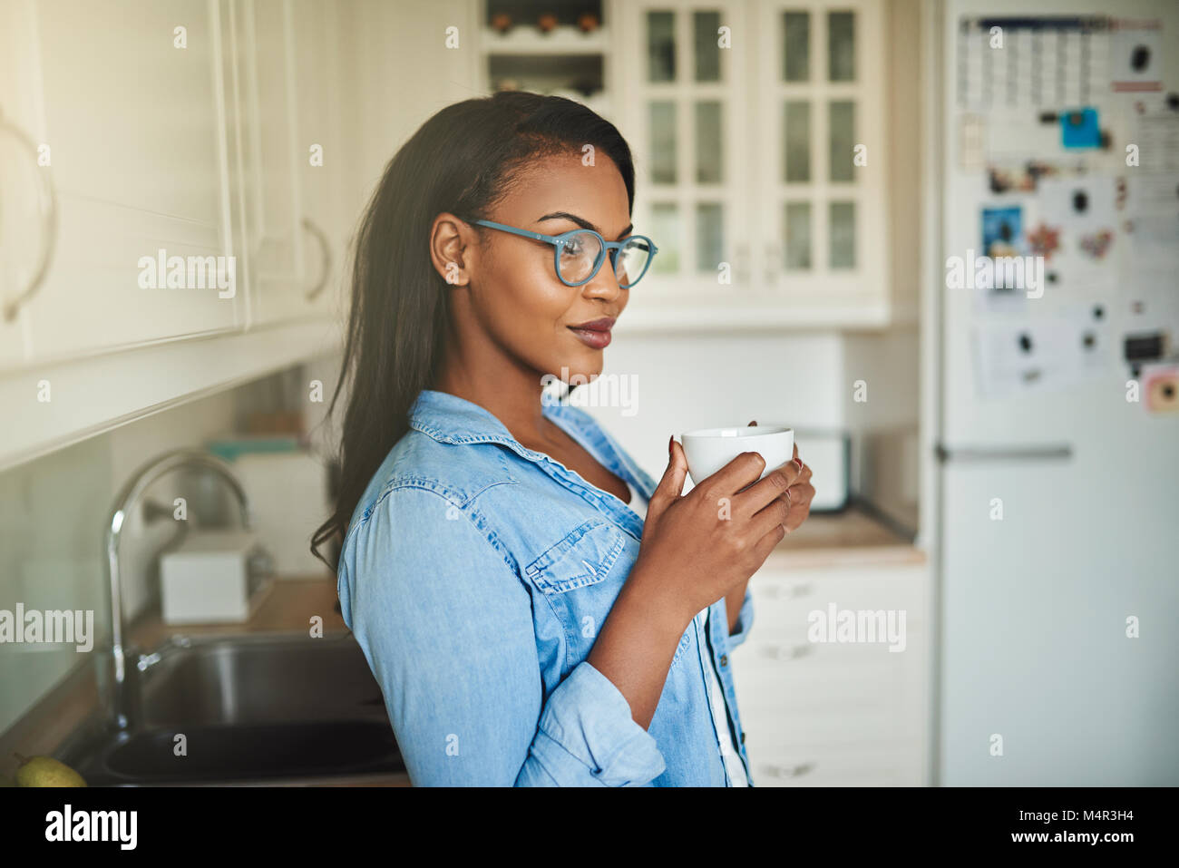 Young African woman deep in thought while standing alone in her kitchen at home drinking a cup of fresh coffee Stock Photo